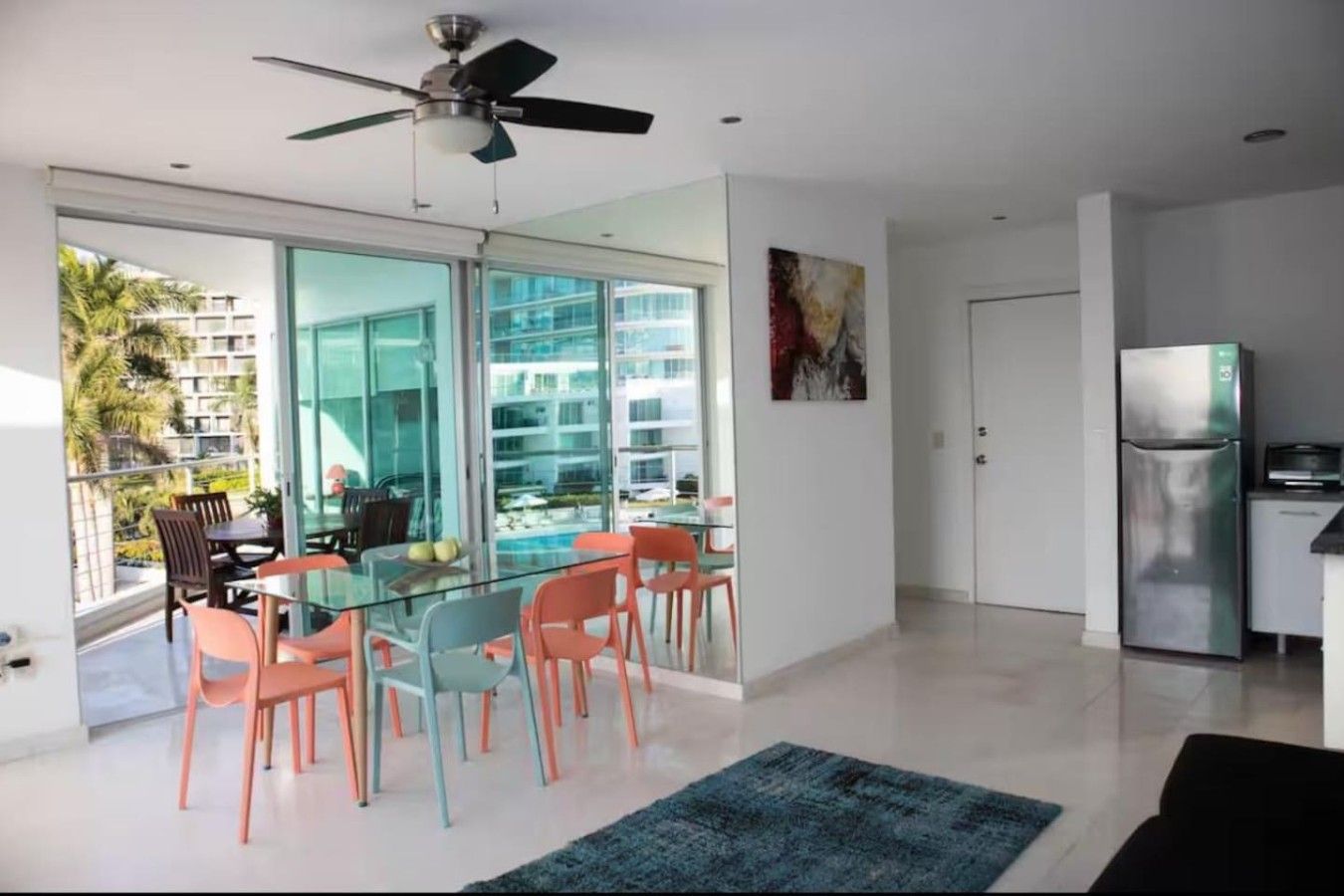 Cozinha moderna com geladeira, área de jantar com mesa e cadeiras de vidro, e ventilador de teto.