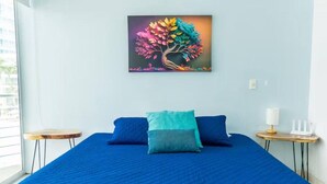 Una stanza con un letto, due cuscini, un comodino, una lampada e un quadro di un albero appeso al muro.