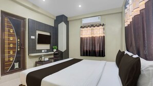 A hotel room with a bed, a desk with a computer, a TV, and a window with curtains. - Super Hotel O New Marine Drive Puri (Puri)