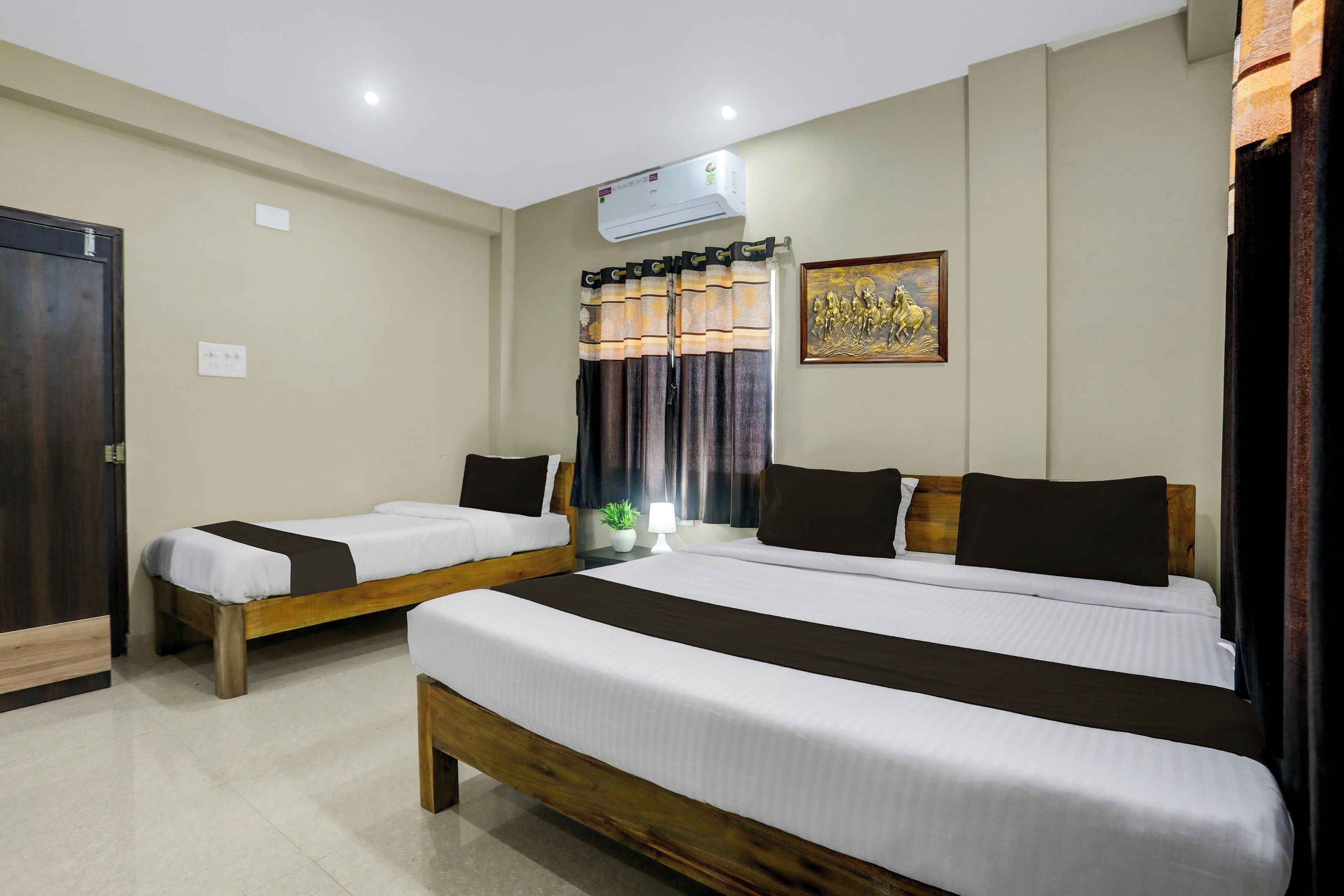A hotel room with two single beds, a wooden headboard, a wall-mounted air conditioner, and a decorative painting.