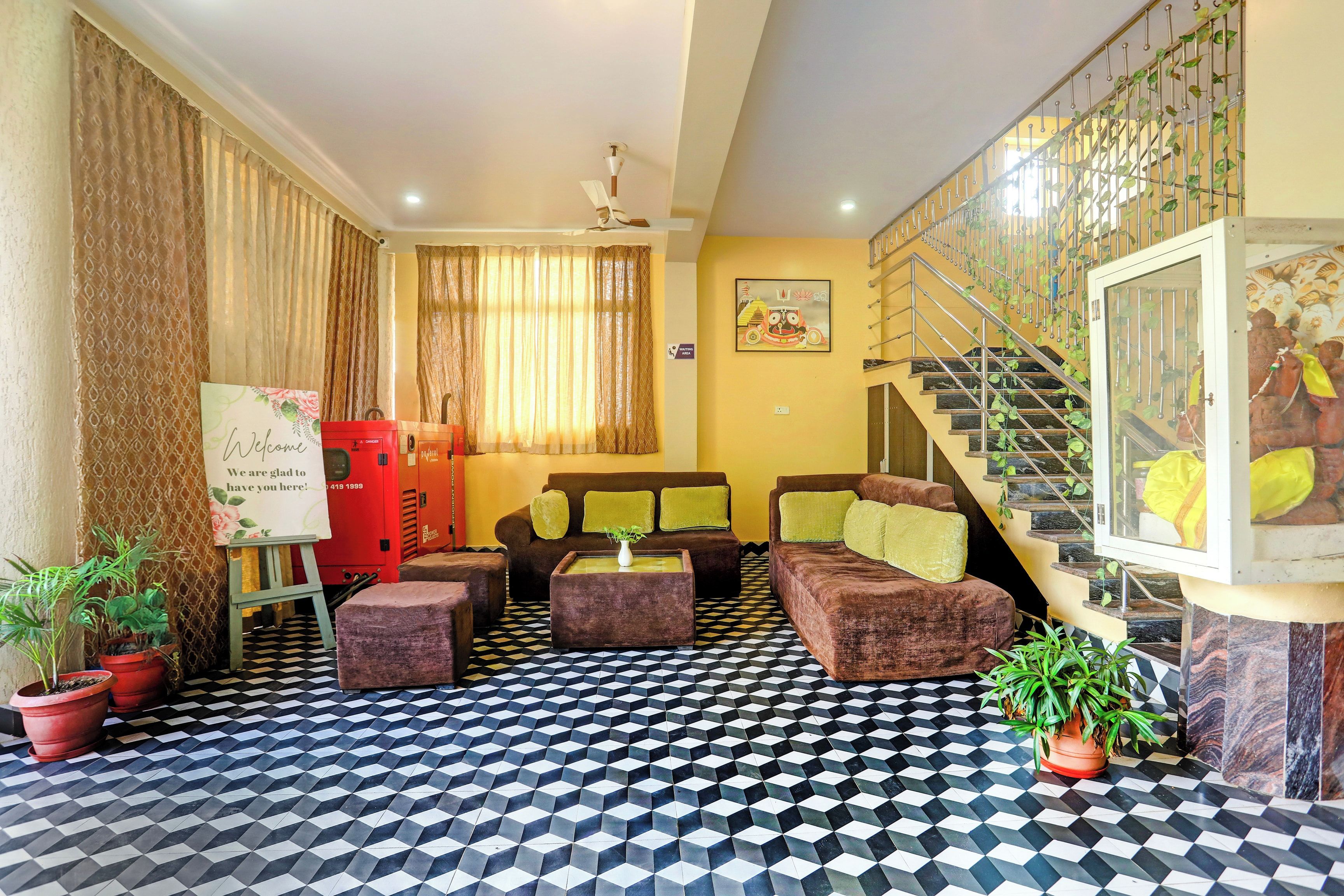A hotel lobby with a check-in counter, a staircase with greenery, a sofa set, and a patterned floor.