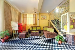 Un vestíbulo de hotel con mostrador de recepción, una escalera con plantas, un conjunto de sofás y un suelo con diseño.