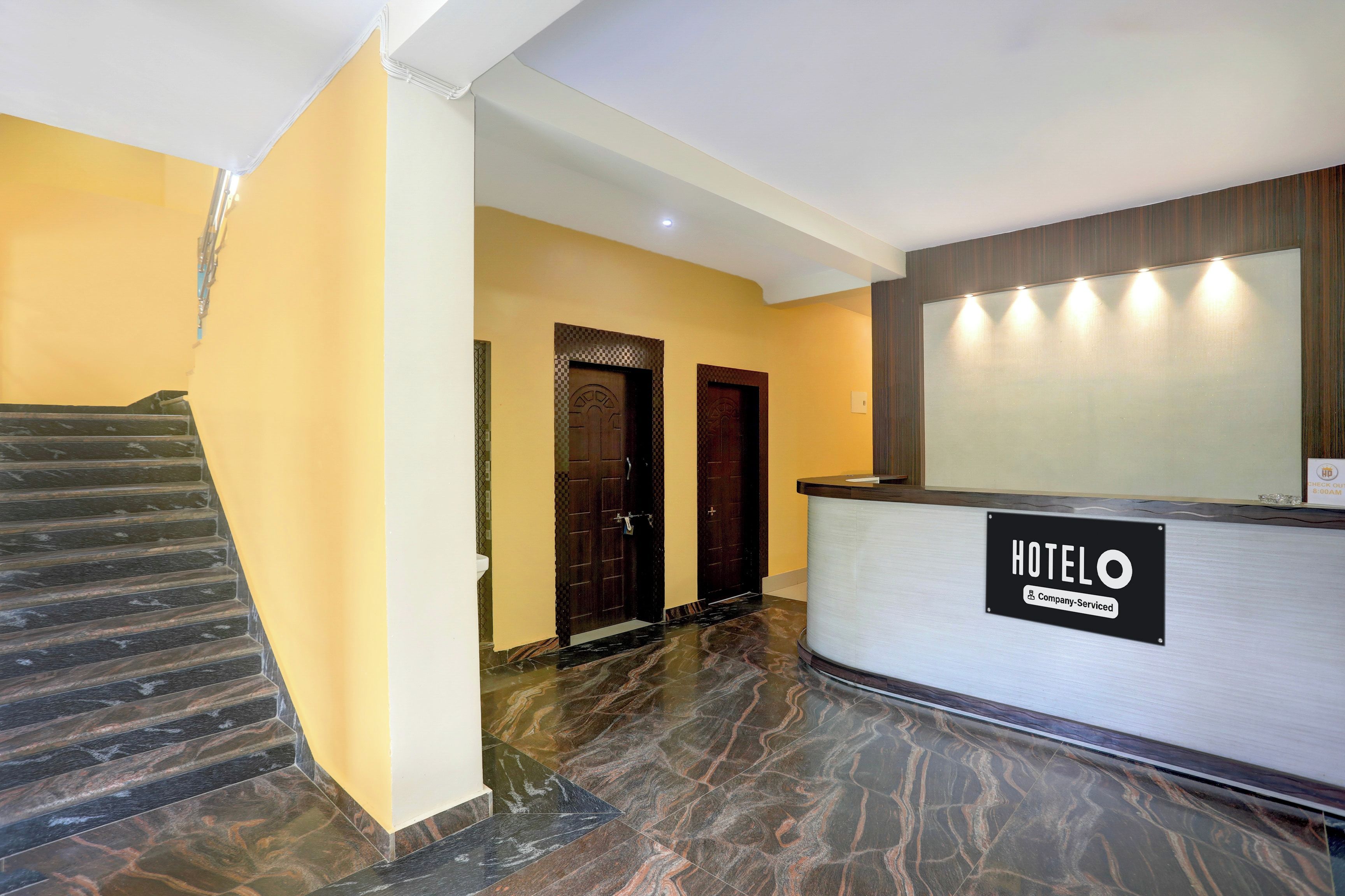 A hotel reception area with a marble staircase, a reception desk, and two doors.