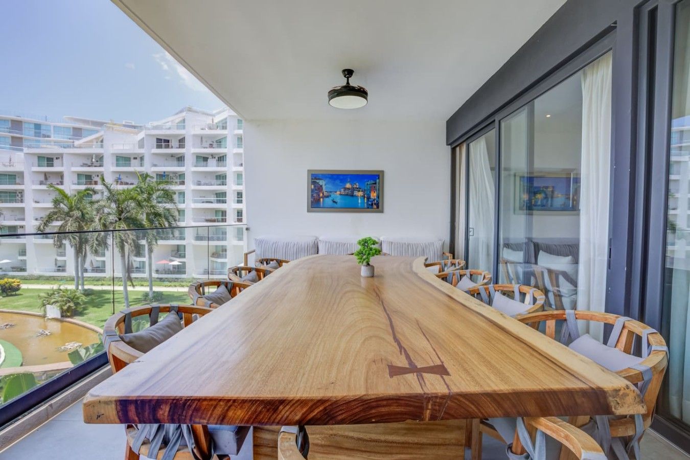 A spacious balcony with a wooden table and chairs, a potted plant, and a cityscape view.
