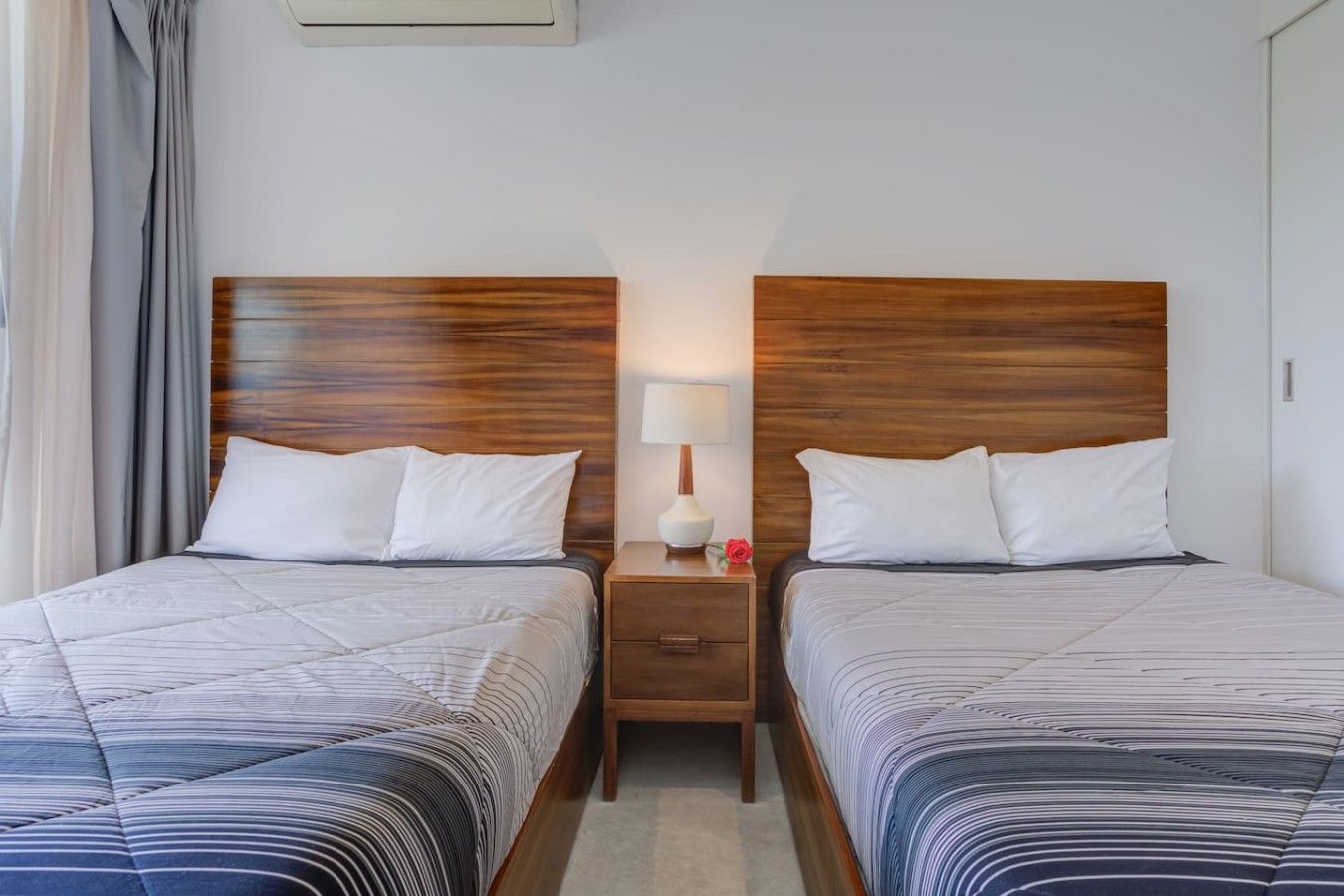 A hotel room with two beds, a nightstand with a lamp, and a window with curtains.