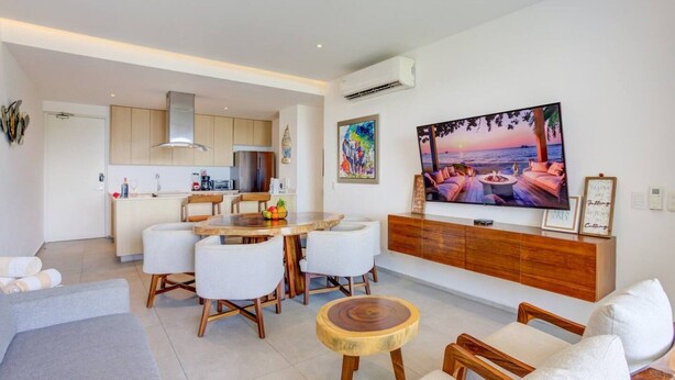 A modern living room with a dining area, a large flat-screen TV, and a kitchen in the background. - 406 Increible depa con jacuzzi priv y vista al mar (Nuevo Vallarta)