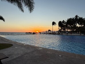 A swimming pool at sunset with palm trees and a beach in the background. - Depto. Playa Vista Mar Villa Magna Nuevo Vallarta (Nuevo Nayarit)