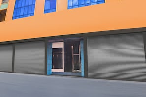 A building with a large orange facade, a central entrance with a glass door, and two closed roller shutters on either side. - Hotel O Rayagada Downtown (Rayagarha)