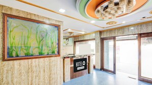 A hotel reception area with a marble wall, a large floral painting, a reception desk, and a modern ceiling design. - Hotel O Rayagada Downtown (Rayagada)