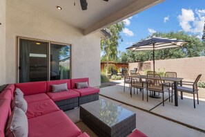 A covered patio with a red sectional sofa, a glass-top coffee table, and a dining set. - Prana Hacienda Near U of A Fire Pit Garden (Tucson)