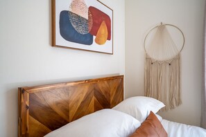 Ein Bett mit Holz Kopfteil, weißen Kissen und einer Wanddekoration aus Makramee.