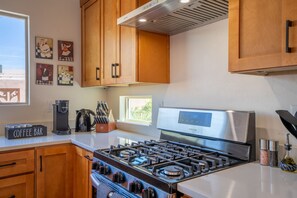 A kitchen with wooden cabinets, a stainless steel stove, a coffee bar, and artwork on the wall. - Prana Hacienda Near U of A Fire Pit Garden (Tucson)