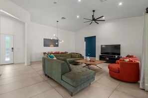 Ein modernes Wohnzimmer mit einer Eckcouch, einem roten Sessel, einem Couchtisch, einem Flachbildfernseher und einem Deckenventilator.