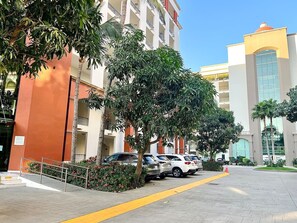 A multi-story building with a parking area, trees, and a clear sky. - Departamento/Estudio en Playa Royale, Nuevo Vta. (Nuevo Vallarta)