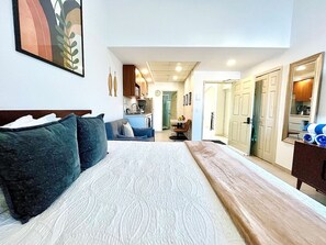 A bedroom with a large bed, a dresser, and a view into the kitchen area. - Departamento/Estudio en Playa Royale, Nuevo Vta. (Nuevo Vallarta)