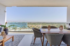 Ein Balkon mit Esstisch und Stühlen, einem Blumentopf und Blick auf ein modernes Gebäude und die Landschaft.