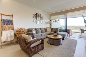 Una sala de estar moderna con un sofá gris, un sillón de mimbre, una mesa redonda y un balcón con vistas.