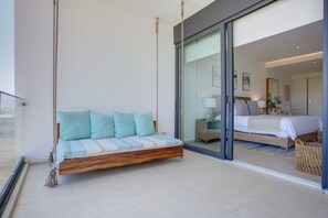Un dormitorio con cama, una silla colgante y vistas a otra habitación a través de una puerta de cristal.