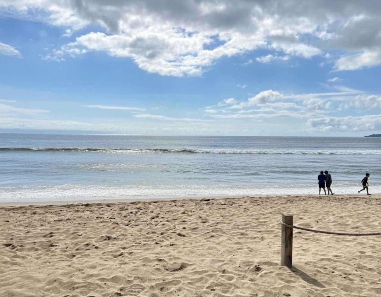 A beach with a sandy shore, a wooden post, and a few people walking.
