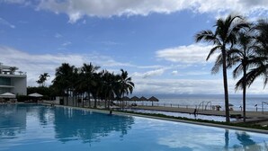 Una piscina con vista sull'oceano, palme e ombrelloni.