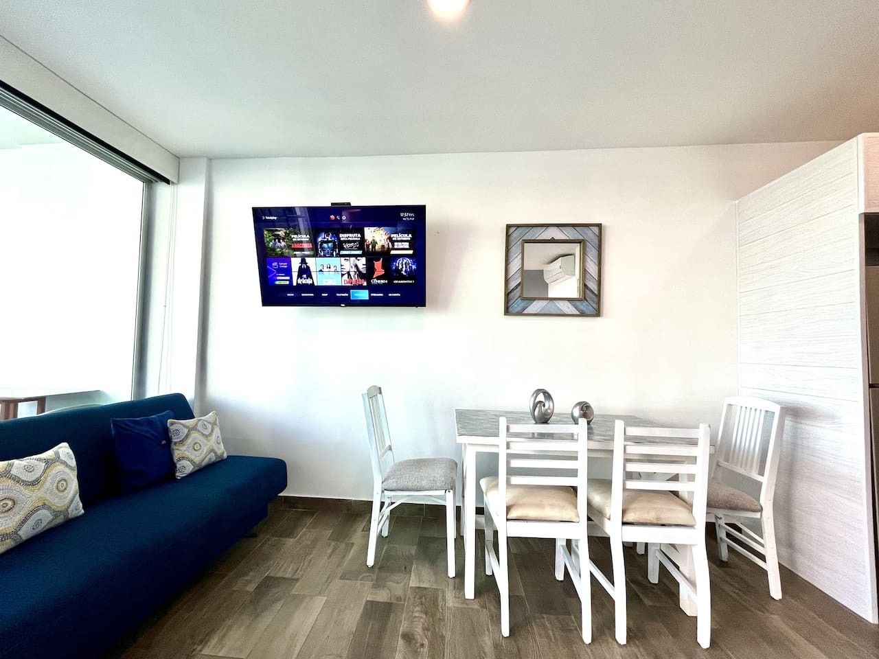 A living area with a sofa, dining table, chairs, a flat-screen TV, and a framed picture on the wall.