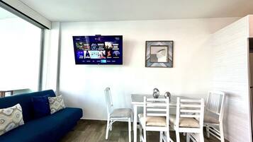 A living area with a sofa, dining table, chairs, a flat-screen TV, and a framed picture on the wall.