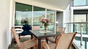 Un balcone con un tavolo e sedie in vetro, un vaso con fiori e vista sulla città.