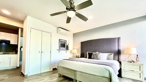 Una camera da letto con un letto, comodini, una ventola a soffitto e vista sulla cucina.