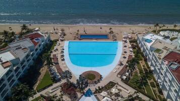 An aerial view of a resort with a central swimming pool, beachfront, and multiple hotel buildings.