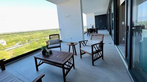Un balcone con vista su vegetazione e una strada, arredato con sedie di legno, un tavolo e un tavolino rotondo.