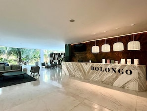 A reception area with a marble counter, hanging pendant lights, and a view of greenery outside. - Luxury Bolongo Beachfront Apartment in Punta Mita (Corral del Risco)