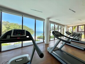 A gym with treadmills and a stationary bike, large windows, and a view of the ocean. - Luxury Bolongo Beachfront Apartment in Punta Mita (Corral del Risco)