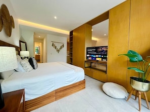 Quarto moderno com cama, mesas de cabeceira, televisão e planta.