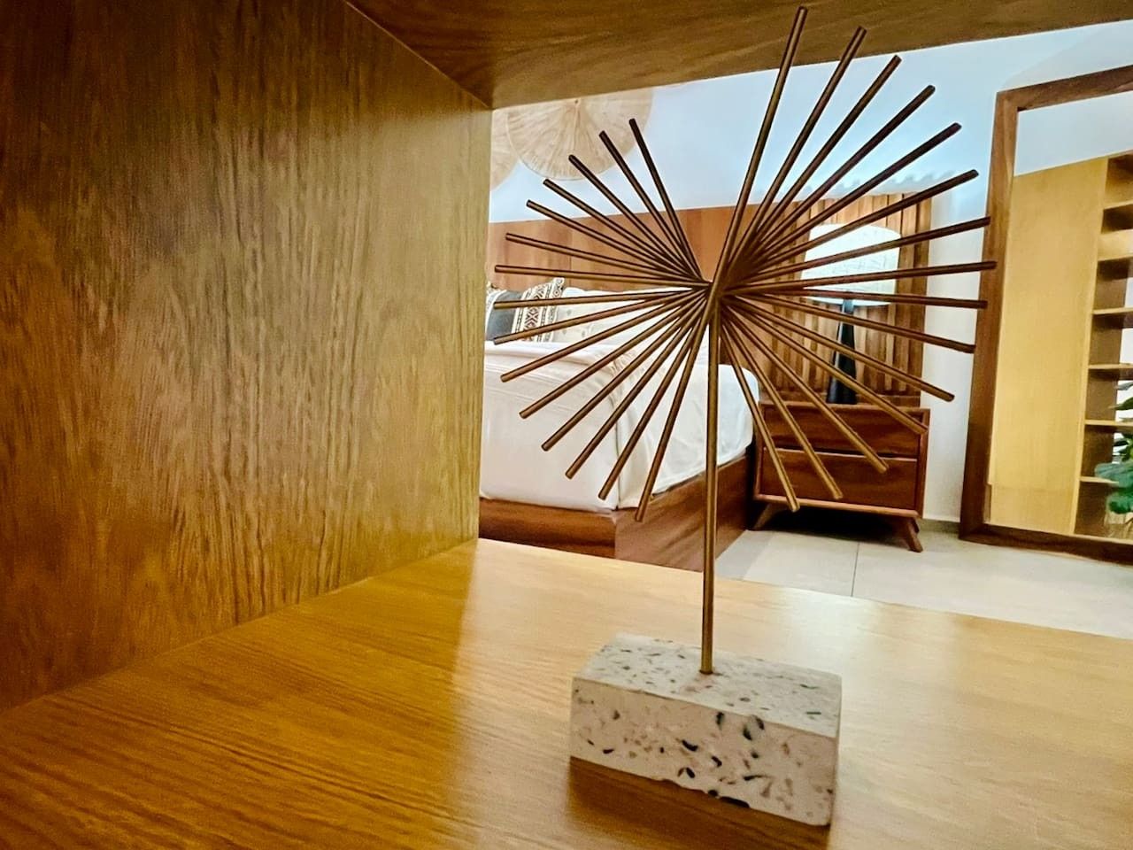 A modern interior with a wooden floor, a central decorative metal piece, and a staircase in the background.