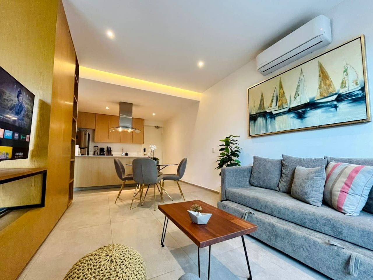 A modern living room with a grey sofa, a wooden coffee table, and a painting of sailboats.