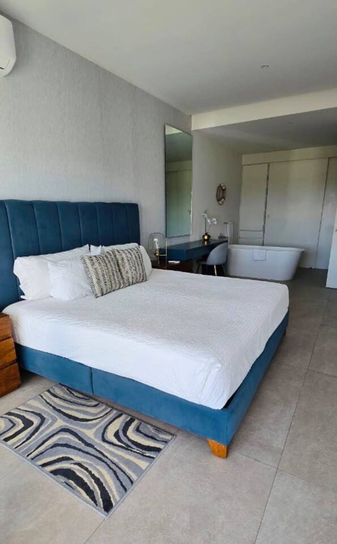 A modern bedroom with a large bed, a desk, and a bathroom in the background.