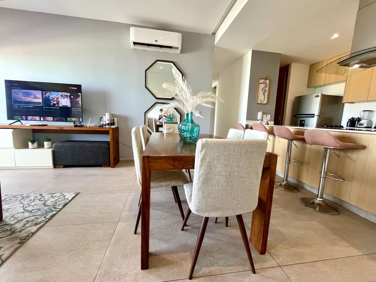 A modern kitchen with a dining area, a TV, and a large mirror.