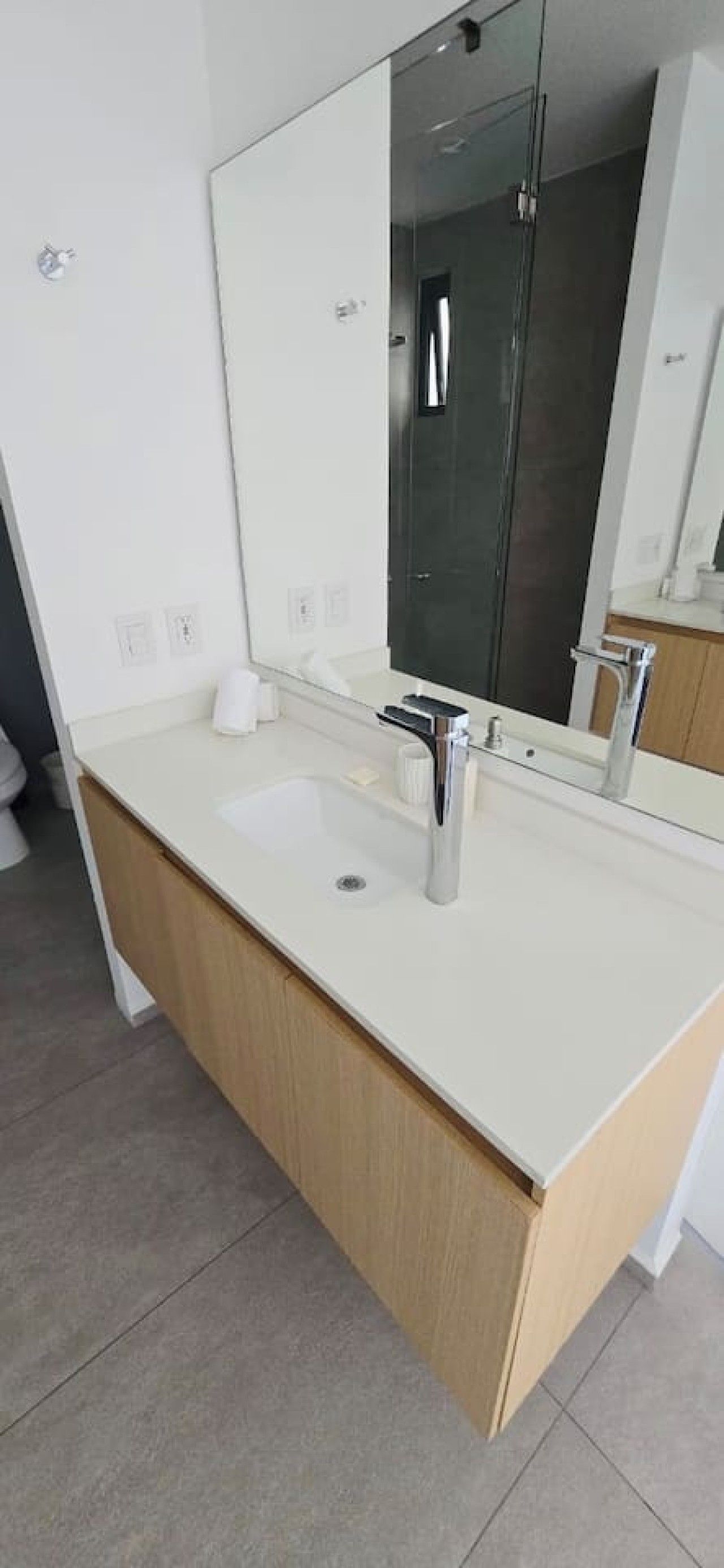 A modern bathroom with a double sink, a large mirror, and a wooden cabinet.