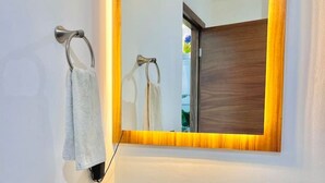 Un bagno con un lavandino rotondo, uno specchio con cornice in legno e due asciugamani appesi ad anelli.