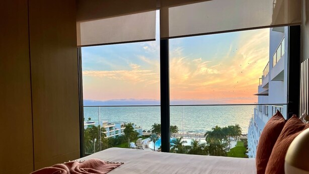 Une chambre d’hôtel dotée d’une grande fenêtre donnant sur une plage et l’océan.
