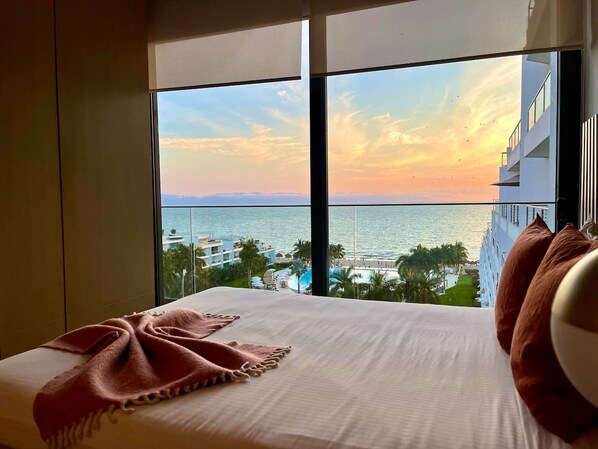 Een hotelkamer met een groot raam met uitzicht op een strand en de oceaan.