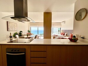 Una cocina moderna con una isla central, horno empotrado y vistas al océano.