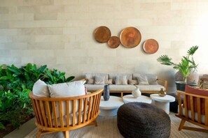A modern living room with a sofa, wooden chairs, round coffee tables, and decorative wall art. - Wake Up to Ocean Views – Aria Nuevo Vallarta (Nuevo Vallarta)