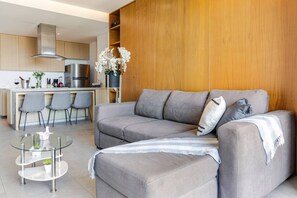 A modern living room with a grey sofa, a glass coffee table, and a kitchen in the background. - Wake Up to Ocean Views – Aria Nuevo Vallarta (Nuevo Vallarta)
