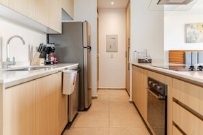 A modern kitchen with wooden cabinets, stainless steel appliances, and a tiled floor. - Wake Up to Ocean Views – Aria Nuevo Vallarta (Nuevo Vallarta)