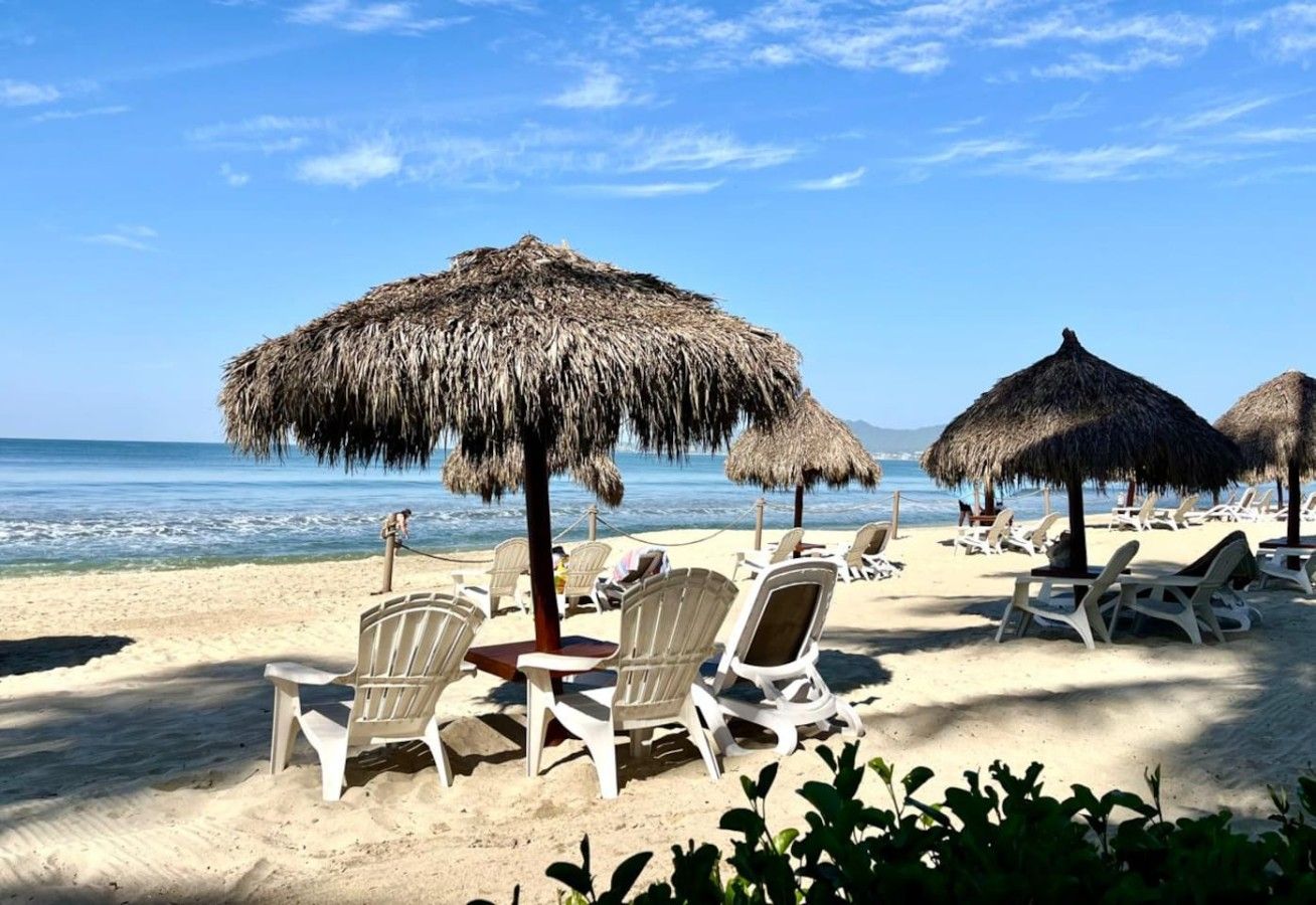 A beach with thatched umbrellas and white lounge chairs.