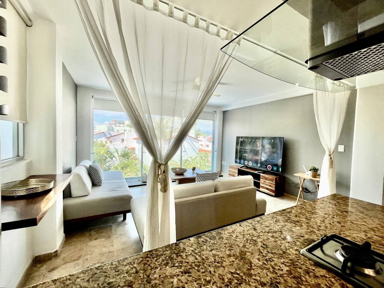 A modern living room with a sofa, a television, and a kitchen area with a granite countertop.