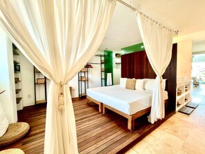 Een slaapkamer met een bed, gordijnen, houten vloeren en uitzicht op een balkon.