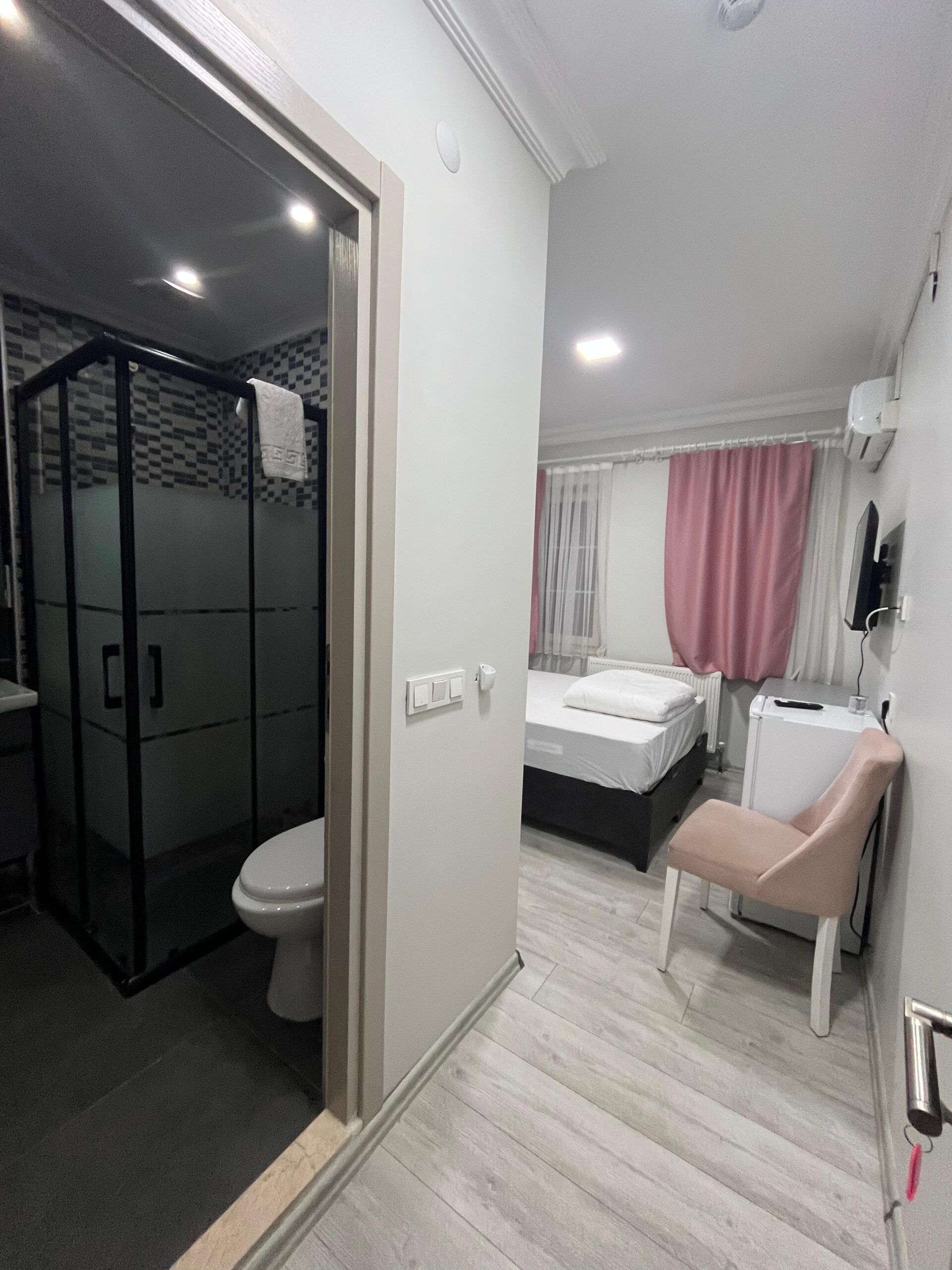 A modern bathroom with a shower enclosure, toilet, and a bed with a pink curtain.
