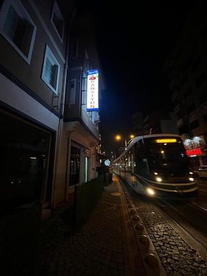 A nighttime street scene with a tram passing by, a building with a sign, and a sidewalk.